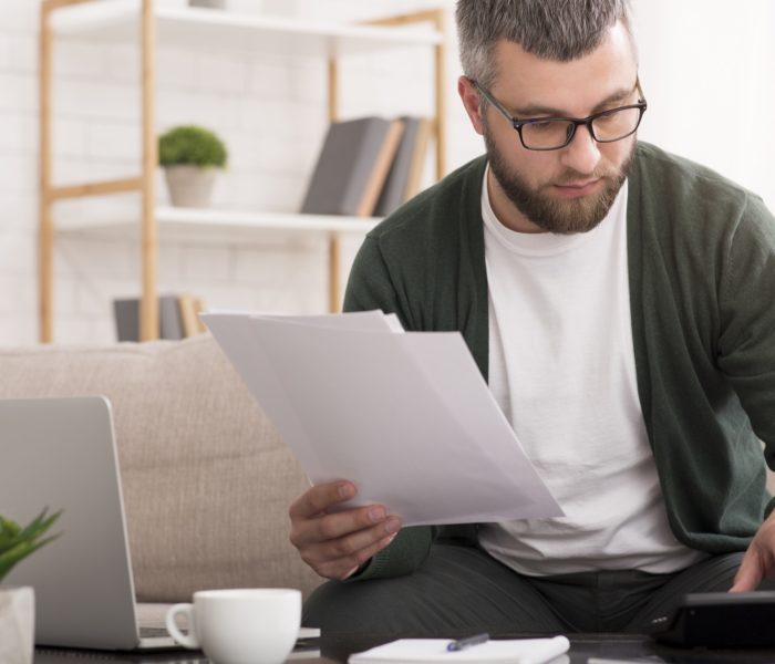 Man with calculator counting money and checking bills at home